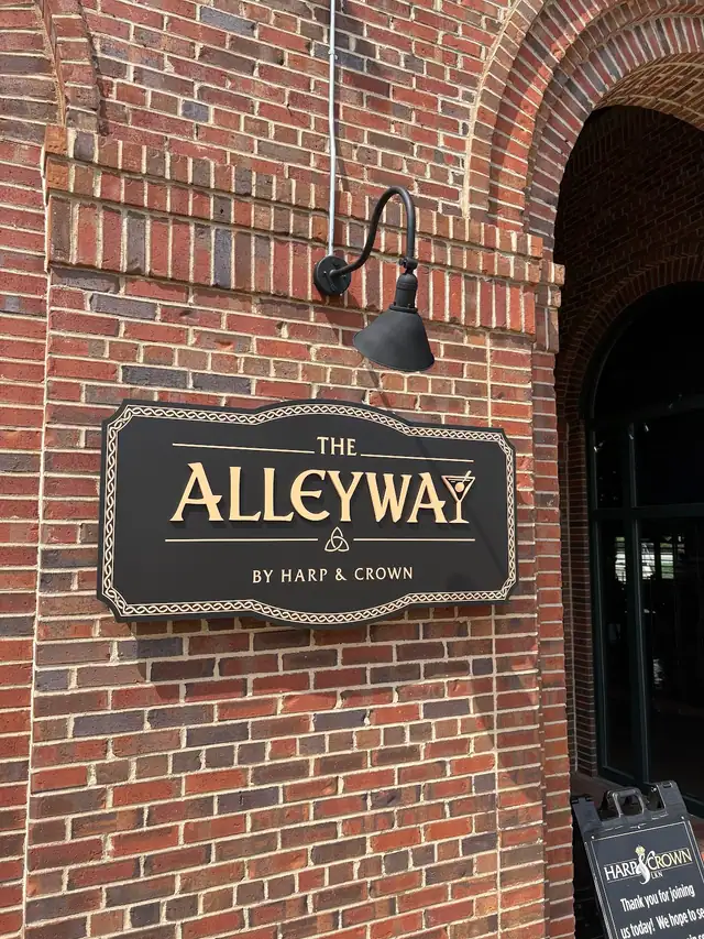 The Alleyway exterior sign on brick with a cocktail-glass letter detail and the line by Harp & Crown.