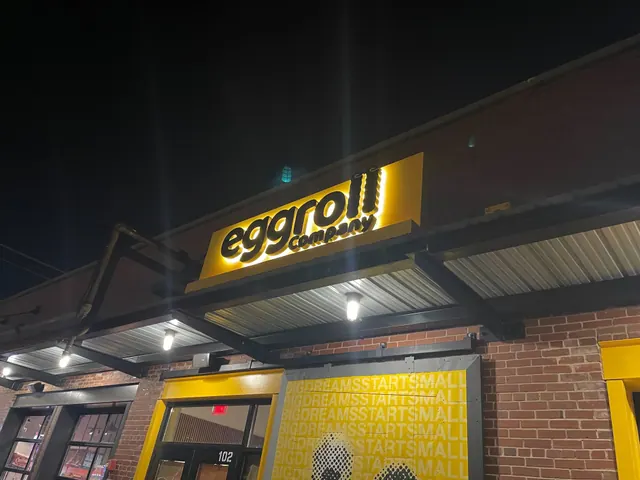 Eggroll Company exterior at night, with illuminated yellow signage and matching entrance and window graphics.